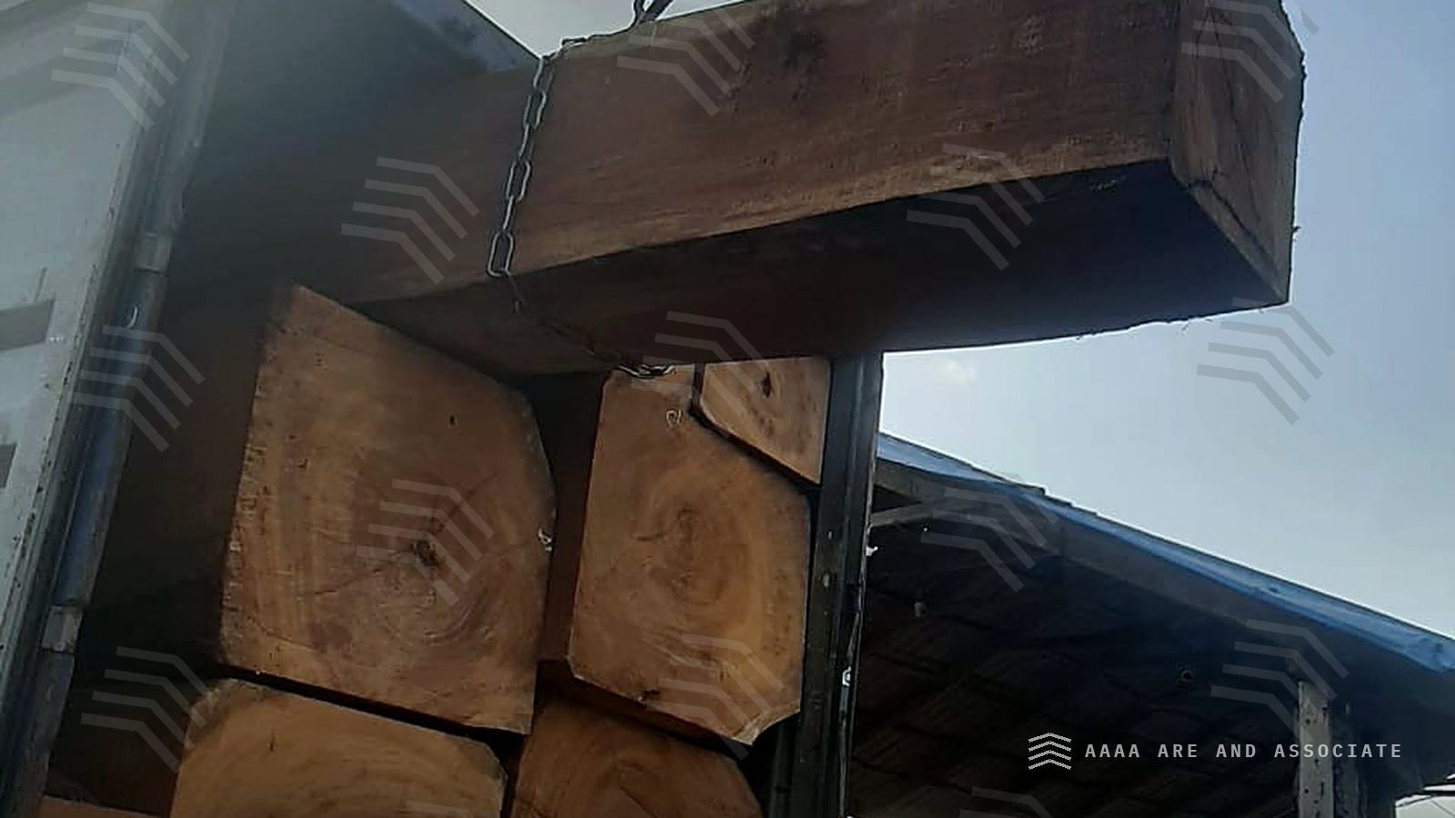 Truck-mounted crane lifting a squared hardwood baulk into a shipping container being loaded at a Nigerian timber yard