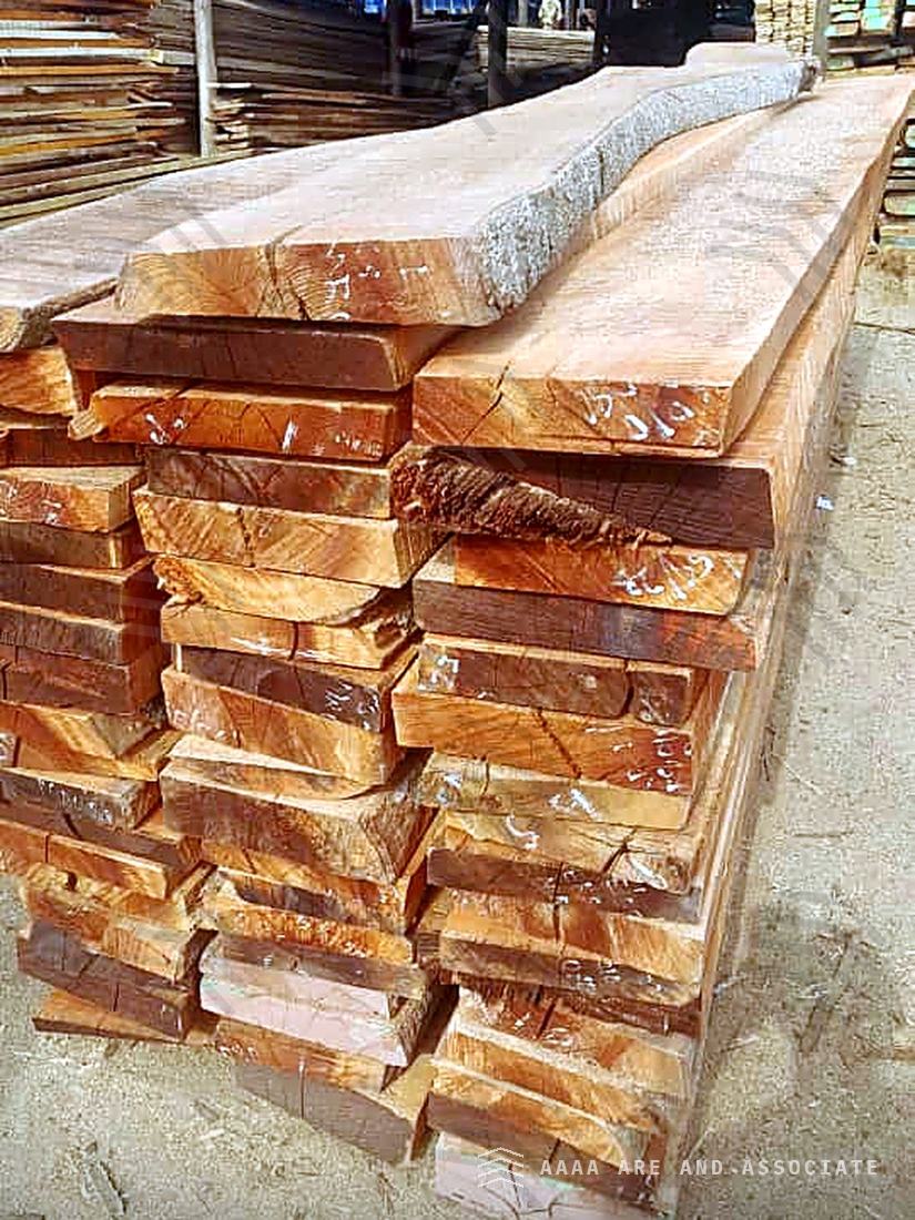 Freshly sawn reddish-brown hardwood boards strip-stacked in long lengths at a sawmill in Nigeria, with further timber stacks behind