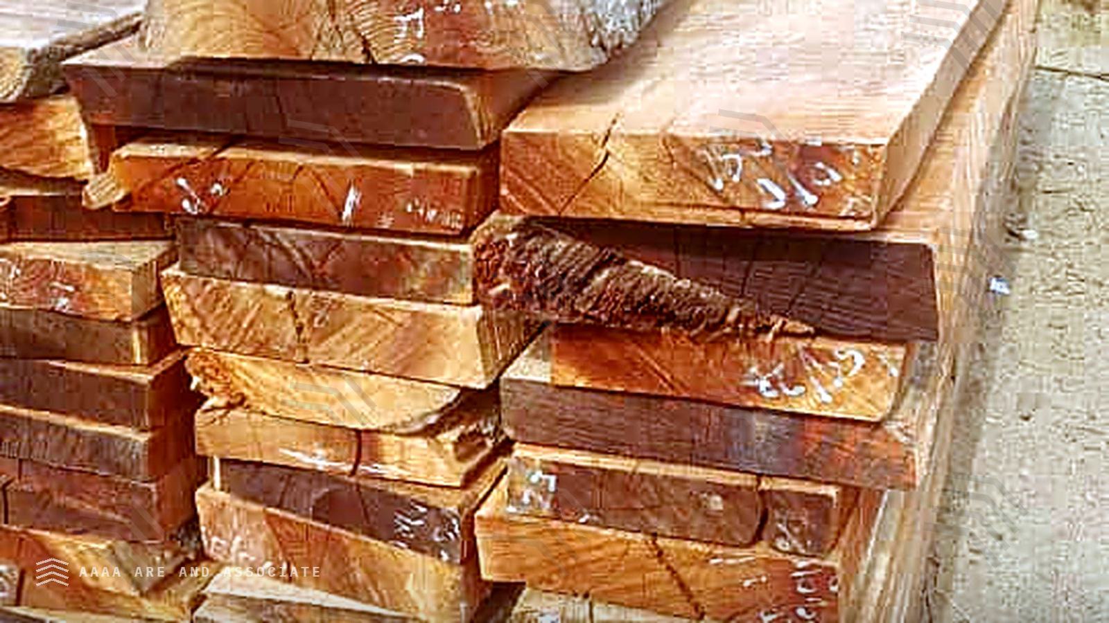 Freshly sawn reddish-brown hardwood boards strip-stacked in long lengths at a sawmill in Nigeria, with further timber stacks behind